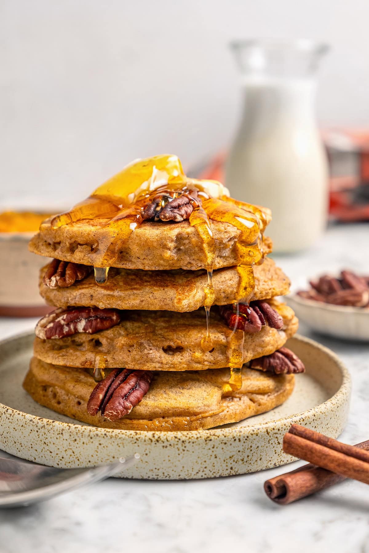 This lightened up version of pumpkin pancakes is also extra fluffy! You'll love the cozy fall flavor in this easy, healthier pancake recipe. Stack of pumpkin pancakes on plate with syrup, pecans, and butter