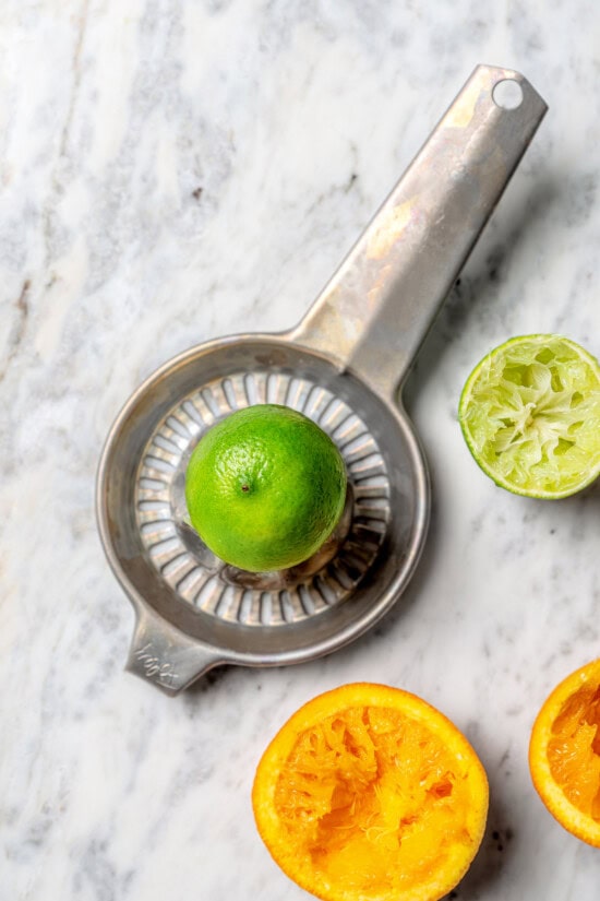 Lime in citrus juicer, with juiced lime and orange halves
