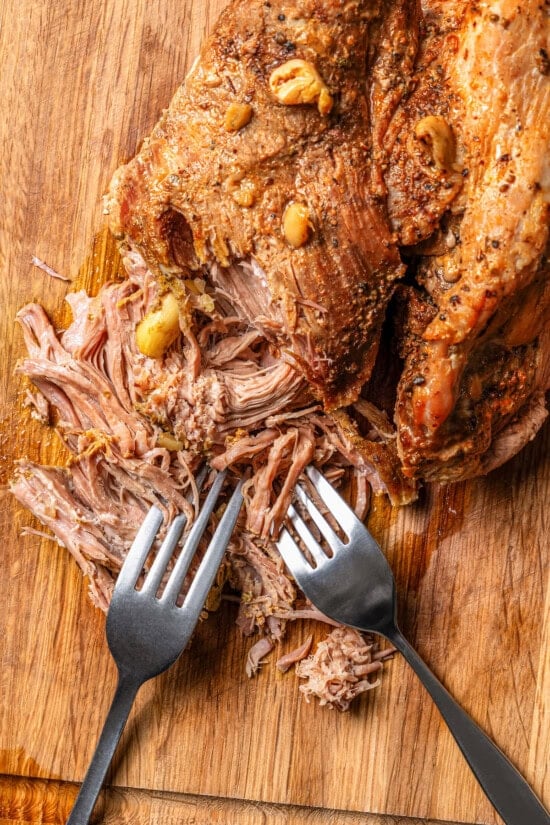 Partially shredded pernil on cutting board with forks