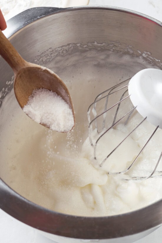 Pavlova is an elegant, light dessert that pairs airy meringue nests with whipped cream and fresh fruit. It's almost too pretty to eat! Spooning sugar into bowl of whipped egg whites