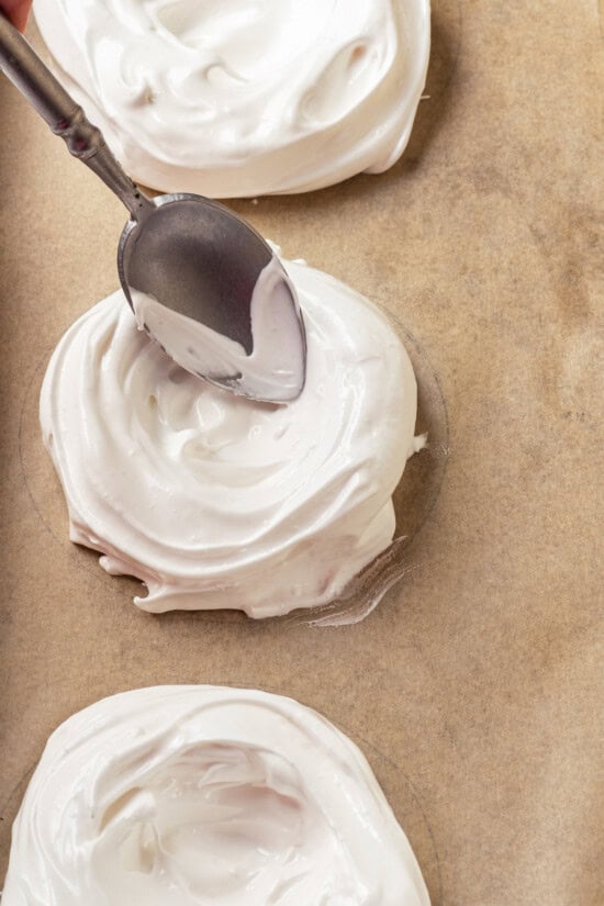 Pavlova is an elegant, light dessert that pairs airy meringue nests with whipped cream and fresh fruit. It's almost too pretty to eat! Using spoon to form meringue nest for pavlova