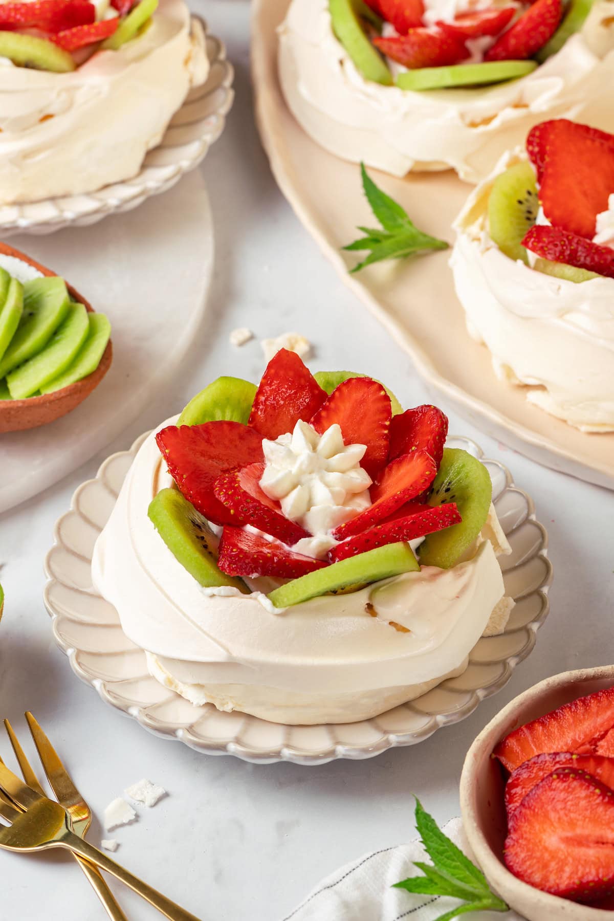 Pavlova is an elegant, light dessert that pairs airy meringue nests with whipped cream and fresh fruit. It's almost too pretty to eat! Strawberry kiwi pavlova on plates and platter