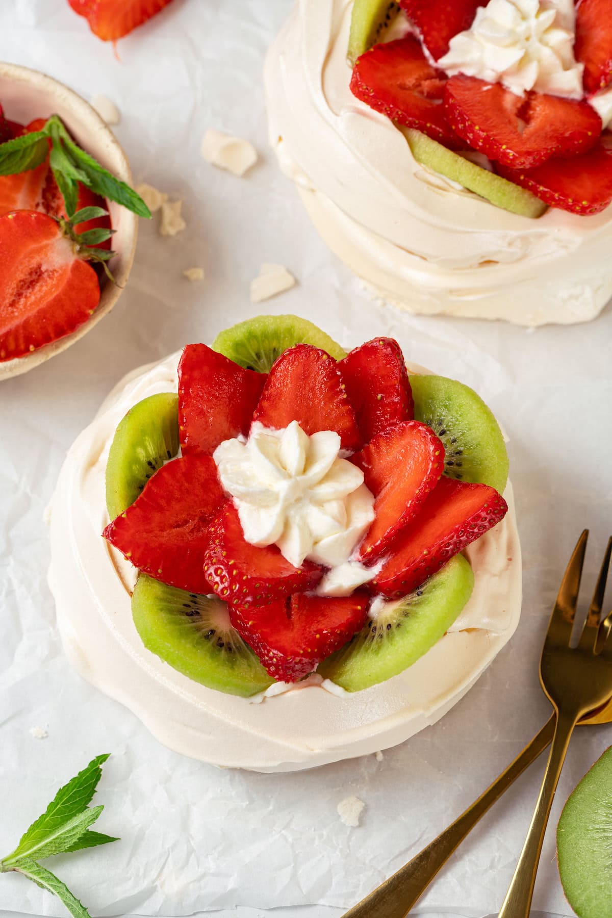 Pavlova is an elegant, light dessert that pairs airy meringue nests with whipped cream and fresh fruit. It's almost too pretty to eat! Top-down view of pavlova with strawberries and kiwi