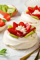 Two pavlova topped with sliced kiwi and strawberries