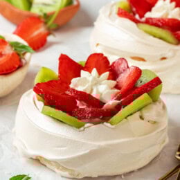 Two pavlova topped with sliced kiwi and strawberries