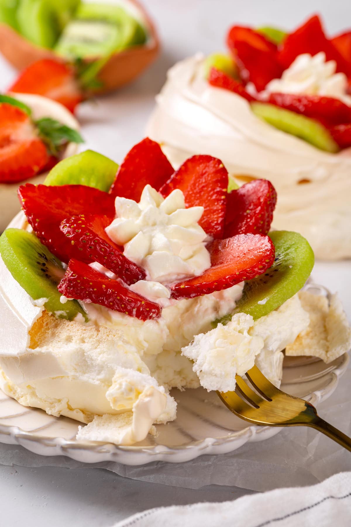 Pavlova is an elegant, light dessert that pairs airy meringue nests with whipped cream and fresh fruit. It's almost too pretty to eat! Fork digging into strawberry kiwi pavlova on plate