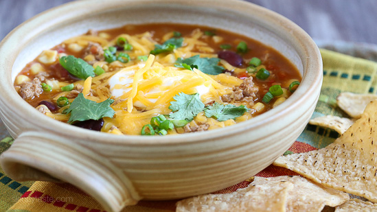 Loaded with beans, ground turkey, tomatoes, and corn, this Easy Taco Soup is hearty, filling, and ready in just 20 minutes! Side view of a bowl of turkey taco soup with sour cream, shredded cheddar cheese, and cilantro.
