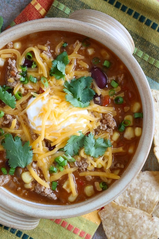 Overhead view of a bowl of taco soup with ground turkey, topped with sour cream, cheese, and cilantro.