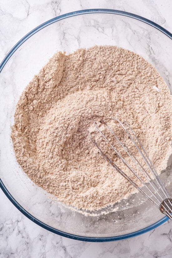 A classic blueberry muffin recipe lightened up with whole wheat flour and applesauce in place of the oil. So moist and delicious! Dry ingredients in glass bowl with whisk