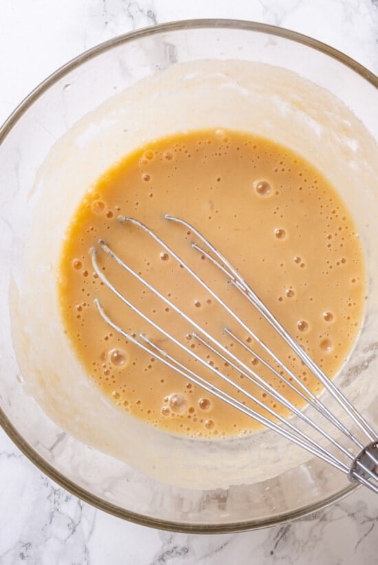 A classic blueberry muffin recipe lightened up with whole wheat flour and applesauce in place of the oil. So moist and delicious! Wet ingredients in glass bowl with whisk