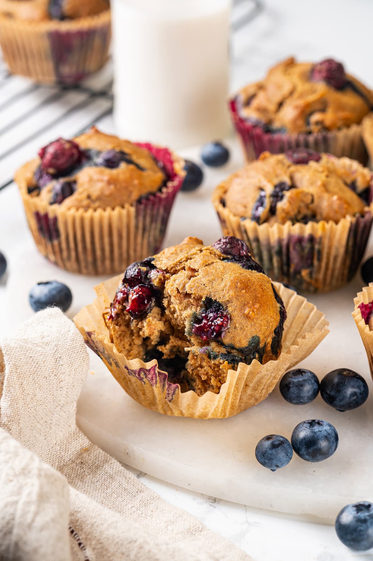 A classic blueberry muffin recipe lightened up with whole wheat flour and applesauce in place of the oil. So moist and delicious! Bitten blueberry muffin in loosened wrapper, with additional muffins in background