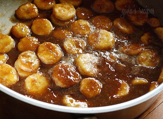 A deep skillet with banana slices cooking in brown sugar sauce
