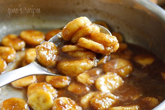 A spoonful of banana slices coated in brown sugar sauce over a saute pan full of banana slices and banana slices and sauce