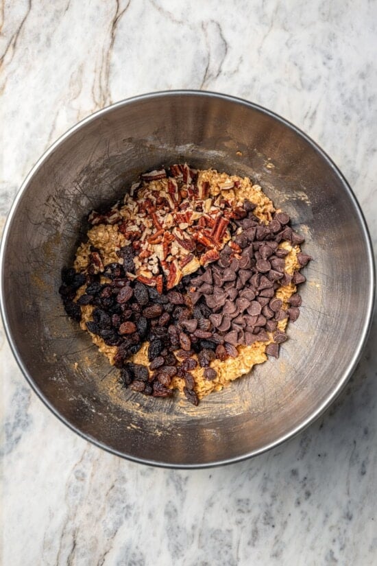 Chewy granola bars are so easy to make at home! This recipe is lighter than other versions and can be customized with your favorite mix-ins. Raisins, chocolate chips, and pecans added to granola bar mixture in bowl.