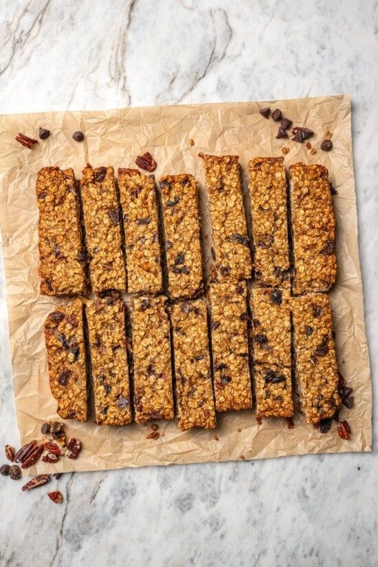 Chewy granola bars are so easy to make at home! This recipe is lighter than other versions and can be customized with your favorite mix-ins. Chewy granola bars cut into pieces on parchment paper.