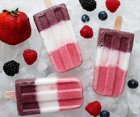 Three striped berry popsicles surrounded by fresh berries