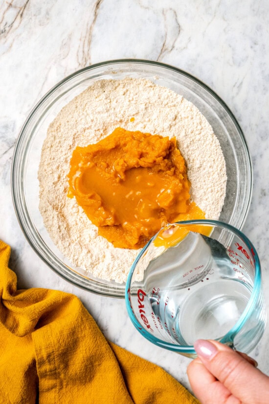 Boxed cake mix makes these pumpkin cupcakes easy to whip up for Halloween parties, Thanksgiving or anytime you want a cozy fall treat! Pouring water into bowl with cake mix and pumpkin puree