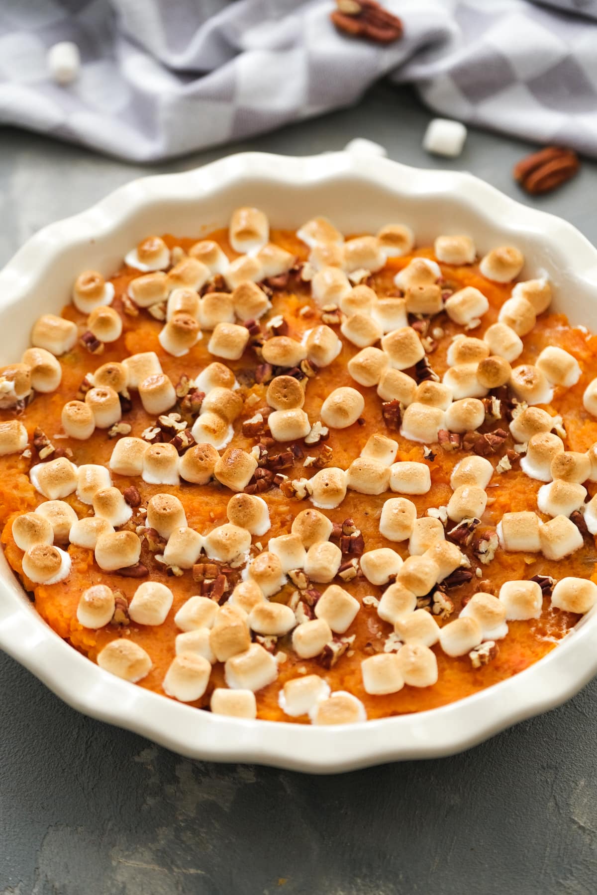 This lighter sweet potato casserole is made with golden raisins, crushed pineapple, and spices, topped with toasty marshmallows and pecans. Overhead view of a sweet potato casserole topped with toasted marshmallows and chopped pecans in a round baking dish.