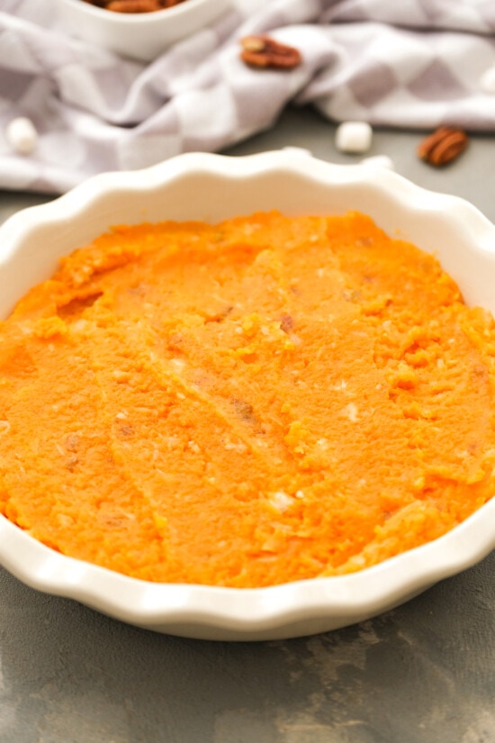 This lighter sweet potato casserole is made with golden raisins, crushed pineapple, and spices, topped with toasty marshmallows and pecans. Mashed sweet potatoes spread inside a round baking dish.