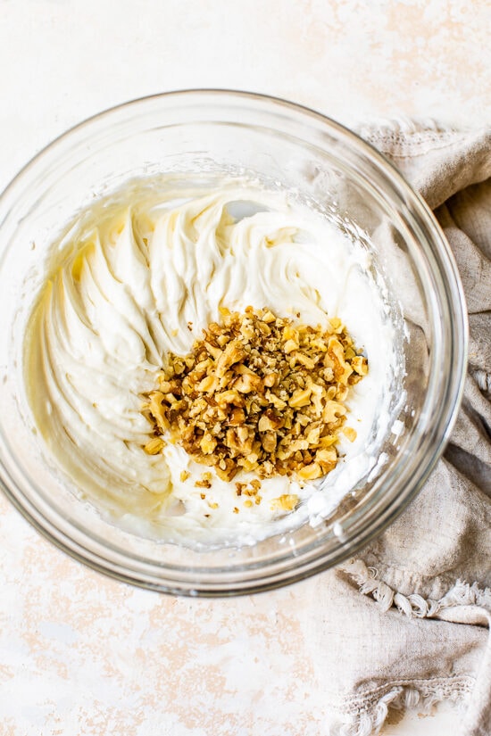 This classic pumpkin roll recipe features an irresistible pumpkin spice sponge cake with a tangy cream cheese filling. Perfect for holidays! Cream cheese filling with walnuts in a bowl