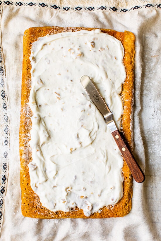 This classic pumpkin roll recipe features an irresistible pumpkin spice sponge cake with a tangy cream cheese filling. Perfect for holidays! Cream cheese filling spread on a pumpkin roll cake