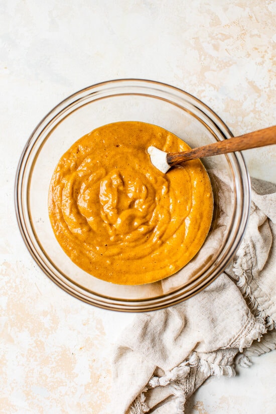 This classic pumpkin roll recipe features an irresistible pumpkin spice sponge cake with a tangy cream cheese filling. Perfect for holidays! A spatula mixing pumpkin roll batter