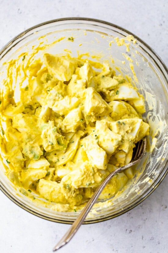 This avocado egg salad uses half the egg yolks and adds lots of healthy fats from avocado. An easy healthy, high protein lunch! Mixing ingredients for avocado egg salad sandwich in a bowl.