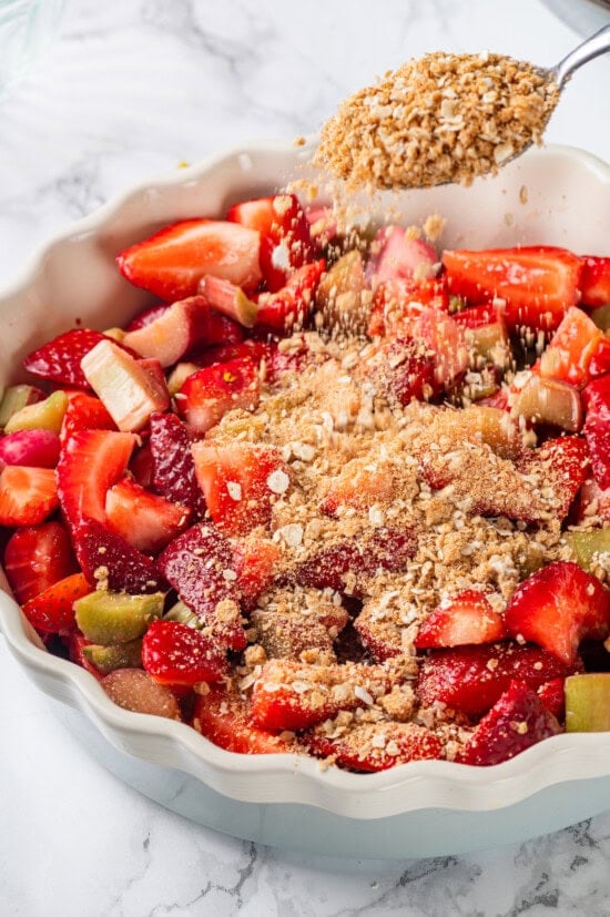 Honey adds the perfect amount of sweetness to the filling in this strawberry rhubarb crisp recipe. Easy to make and impossible to resist! Sprinkling topping onto strawberry and rhubarb filling