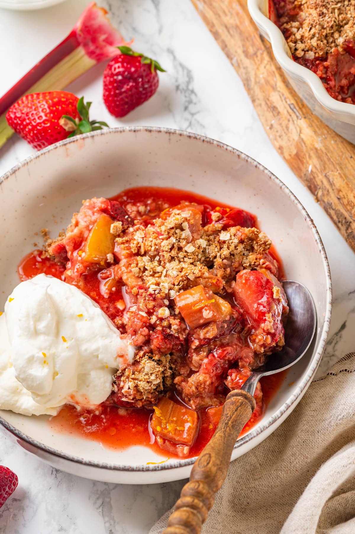 Honey adds the perfect amount of sweetness to the filling in this strawberry rhubarb crisp recipe. Easy to make and impossible to resist! Bowl of strawberry rhubarb crisp with scoop of whipped cream and spoon