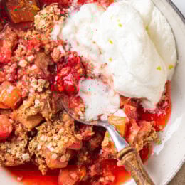 Overhead view of strawberry rhubarb crisp in bowl with whipped cream