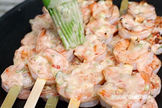 A plate of grilled shrimp on skewers being brushed with creamy chili sauce
