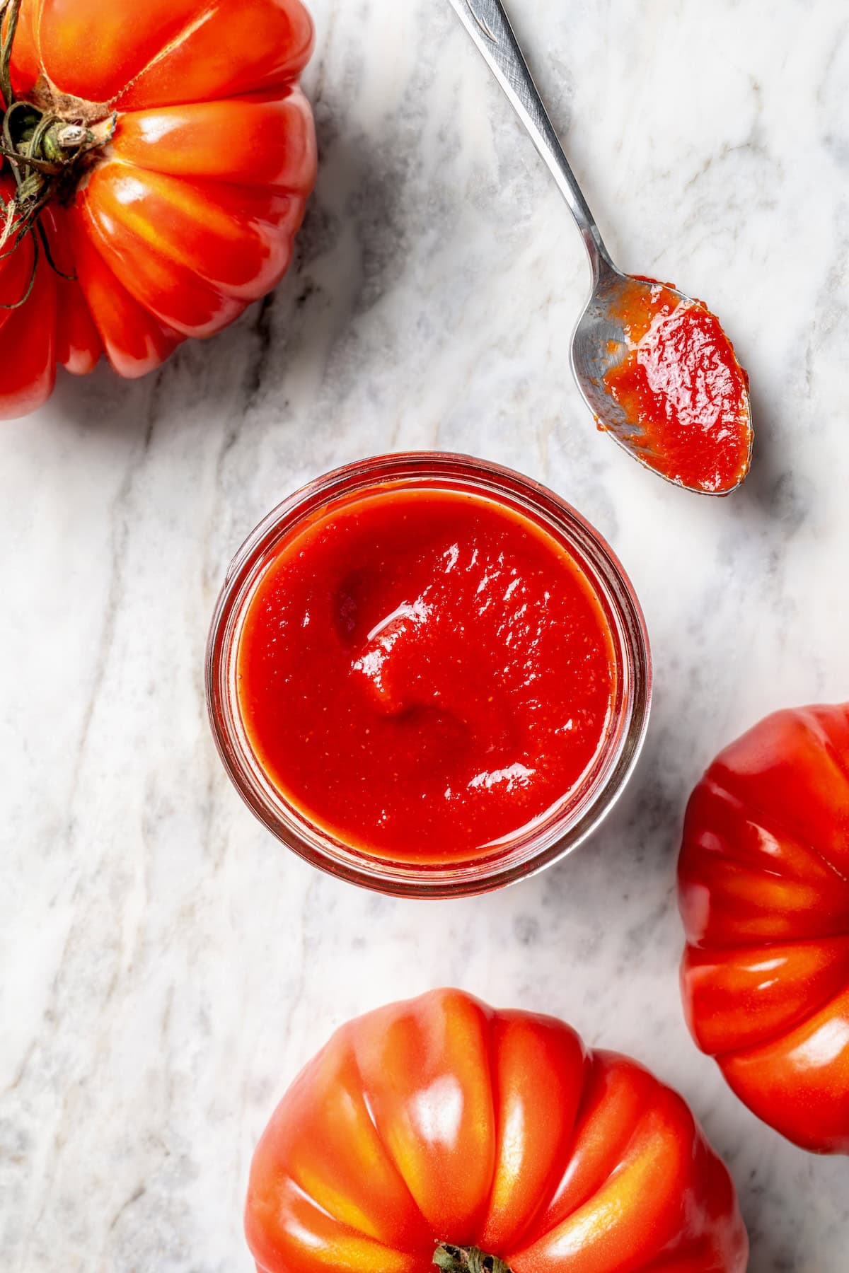 A healthy recipe for homemade ketchup with no high fructose corn syrup. Instead it's sweetened naturally with honey and it tastes amazing! Overhead view of homemade ketchup in jar and spoon, surrounded by fresh heirloom tomatoes