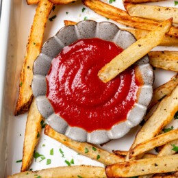 French fry dipping into small bowl of ketchup