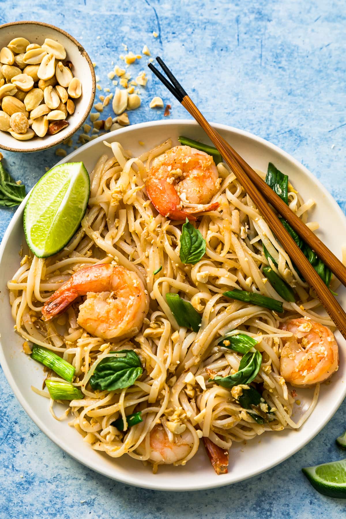 This easy homemade Pad Thai recipe is a lightened up version of the original made with shrimp, eggs, and tofu. Dinner’s done in 25 minutes! Overhead view of shrimp Pad Thai in bowl with lime wedge and fresh basil for garnish