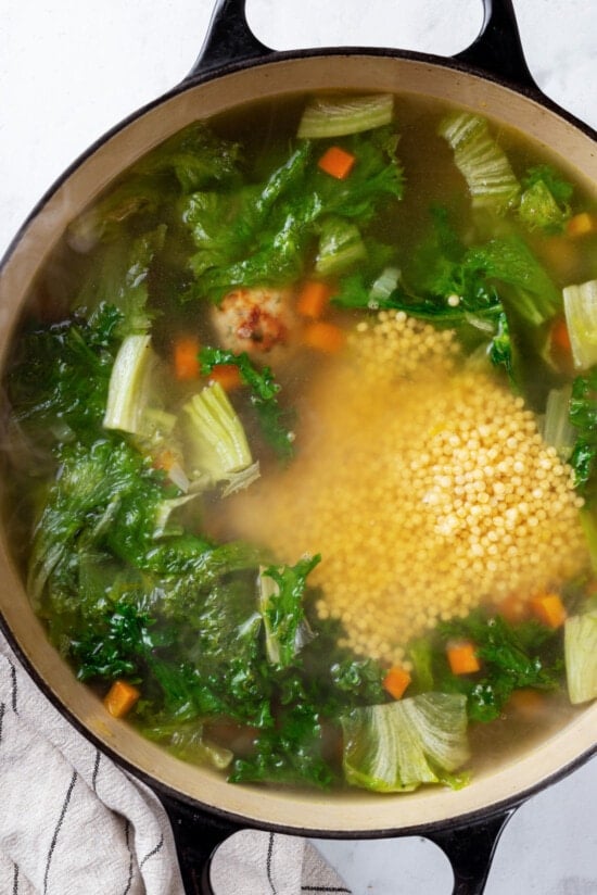 Made with homemade turkey meatballs, tiny pasta, and dark leafy greens, Italian Wedding Soup is simple yet flavorful. Ready in 30 minutes! Greens added to a pot of broth and veggies