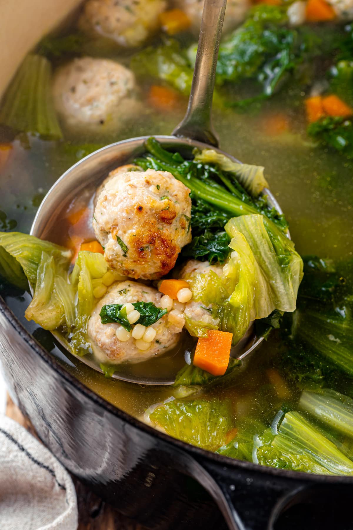 Made with homemade turkey meatballs, tiny pasta, and dark leafy greens, Italian Wedding Soup is simple yet flavorful. Ready in 30 minutes! A ladle of Italian wedding soup over a pot