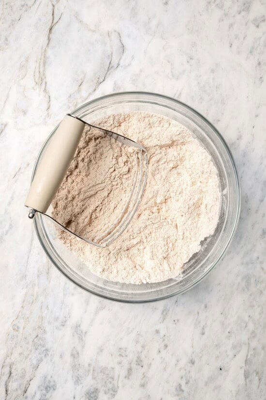 Buttermilk gives these spiced apple scones a moist, tender crumb, while applesauce replaces much of the butter to lighten them up! Overhead view of dry ingredients for apple scones in glass bowl with pastry cutter