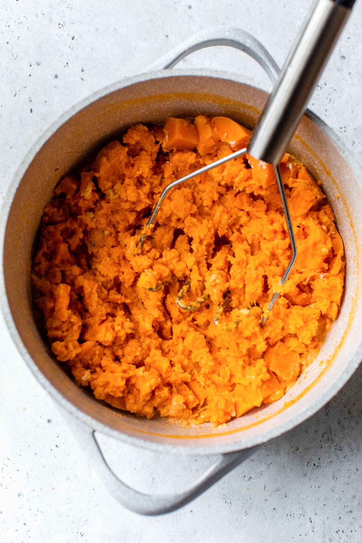 These buttery mashed sweet potatoes are a fluffy, creamy, and delicious side dish recipe. Ready in 25 minutes and made without sugar! Sweet potatoes being mashed in a pot.