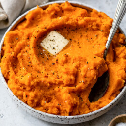 Mashed sweet potatoes topped with a pat of butter in a bow with a spoon.
