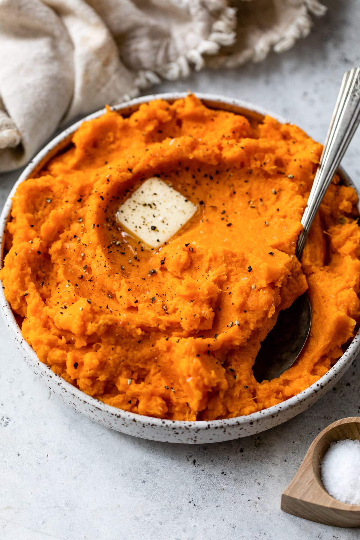 Mashed sweet potatoes topped with a pat of butter in a bow with a spoon.