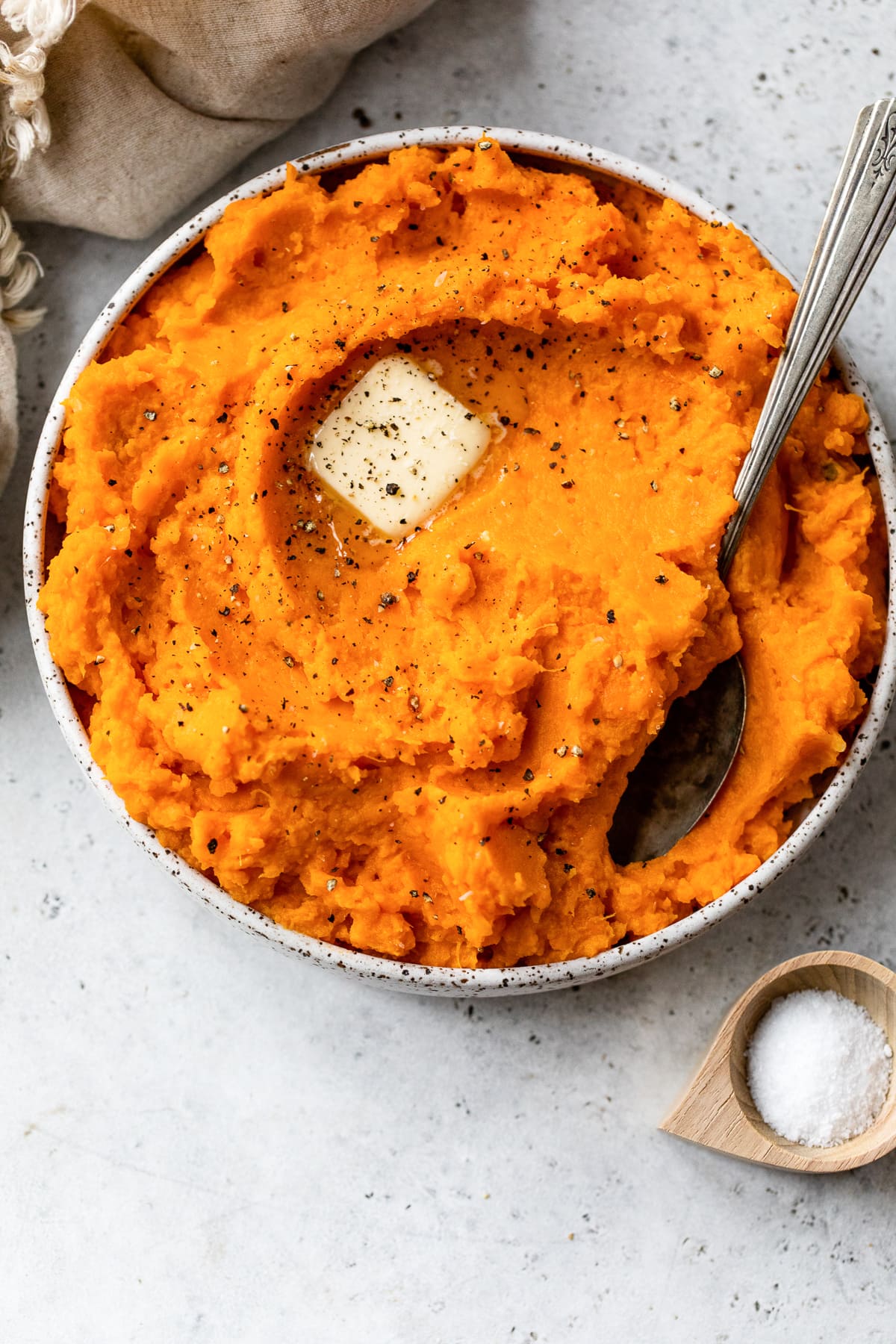 These buttery mashed sweet potatoes are a fluffy, creamy, and delicious side dish recipe. Ready in 25 minutes and made without sugar! Overhead view of mashed sweet potatoes topped with a pat of butter in a bowl with a spoon.