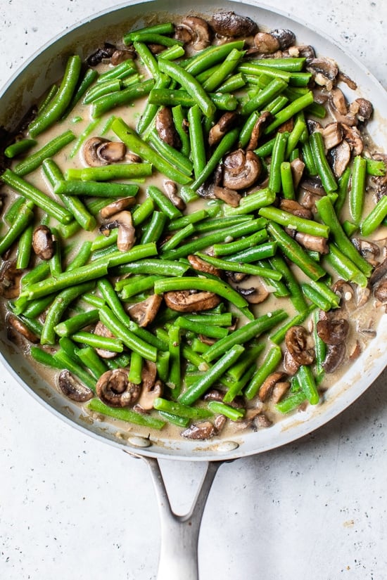 This Green Bean Casserole From Scratch features fresh green beans, cremini mushrooms, shallots, and grated parmesan. green beans and mushrooms in a skillt.