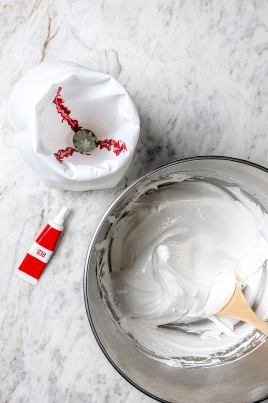 Light and airy peppermint meringues are the perfect addition to any holiday cookie tray! They're surprisingly easy to make and always a hit. Overhead view of meringue in bowl and piping bag painted with red gel food coloring