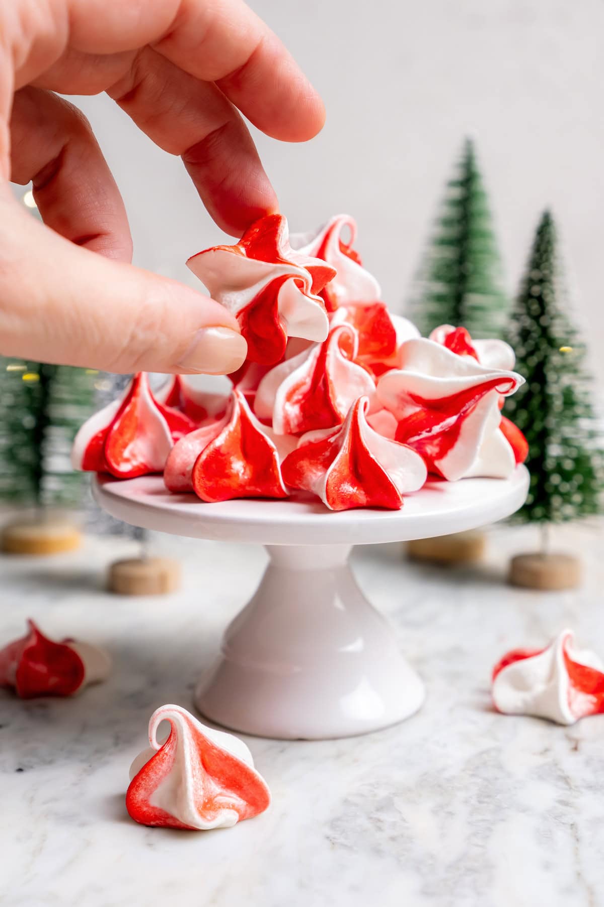 Light and airy peppermint meringues are the perfect addition to any holiday cookie tray! They're surprisingly easy to make and always a hit. Hand taking peppermint meringue from cake stand