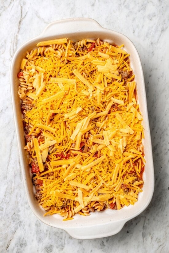 With ground beef, tomatoes, pickles, and cheese, this lightened up cheeseburger casserole recipe is kid-friendly and so delicious! Overhead view of cheese added to cheeseburger casserole before baking