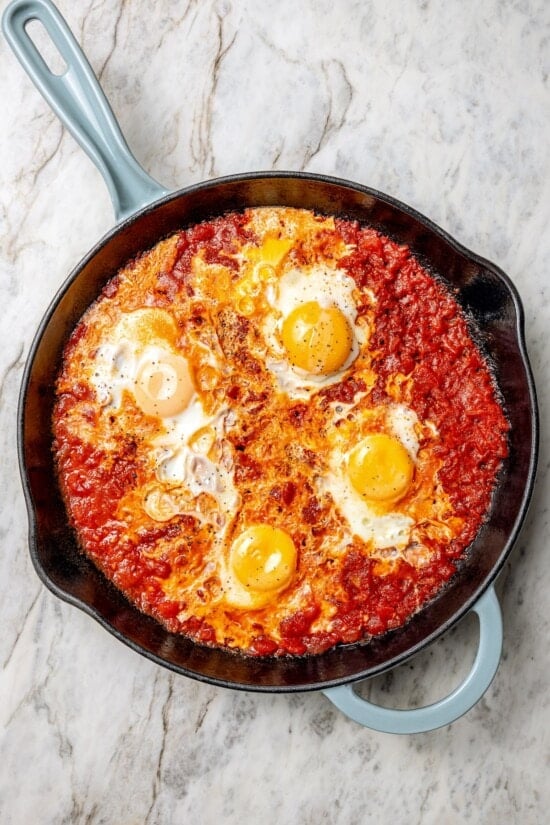 Eggs in purgatory is a simple Italian dish that simmers eggs in a fiery tomato sauce. My version is made with harissa for extra flavor! Overhead view of eggs in purgatory in skillet