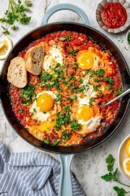 Overhead view of eggs in purgatory in skillet with spoon and 2 slices of bread
