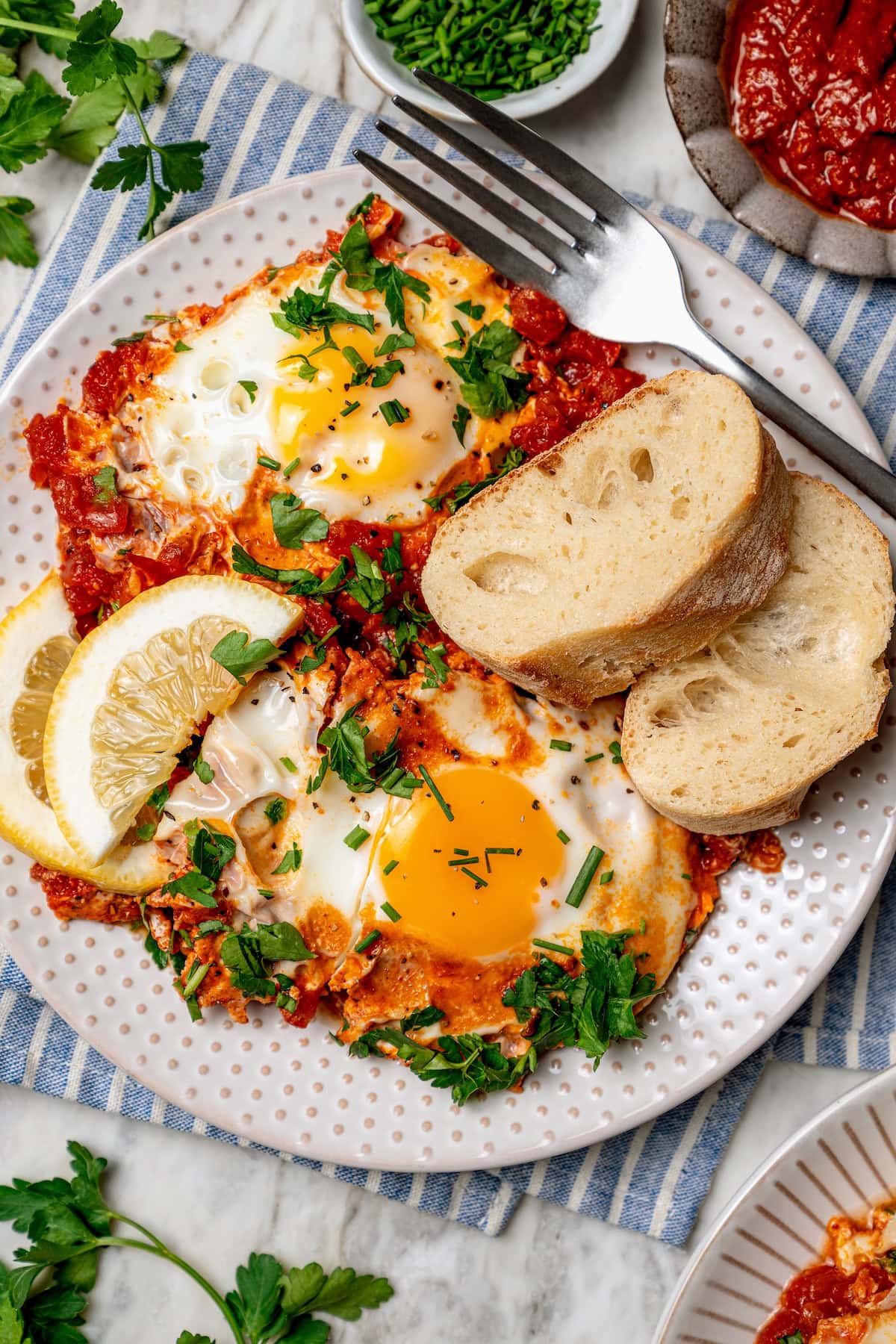 Eggs in purgatory is a simple Italian dish that simmers eggs in a fiery tomato sauce. My version is made with harissa for extra flavor! Overhead view of eggs in purgatory on plate with slices of bread