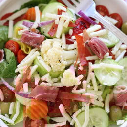 Chopped romaine hearts, shredded mozzarella, olives, prosciutto, turkey pepperoni, roasted red peppers, cucumbers, tomatoes, pepperoncini and Giardiniera (colorful vegetables in vinegar) – this quick Italian antipasto salad requires no cooking, which makes it perfect to whip up or pack for lunch.
