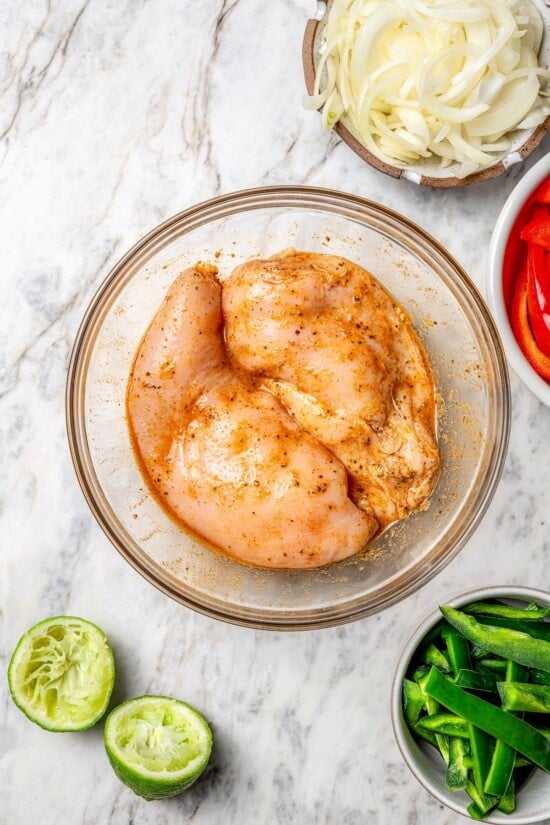 These easy chicken fajitas are made with grilled chicken breast, bell peppers and onions and served sizzling hot with tortillas and cheese! Overhead view of 2 chicken breasts marinating in bowl